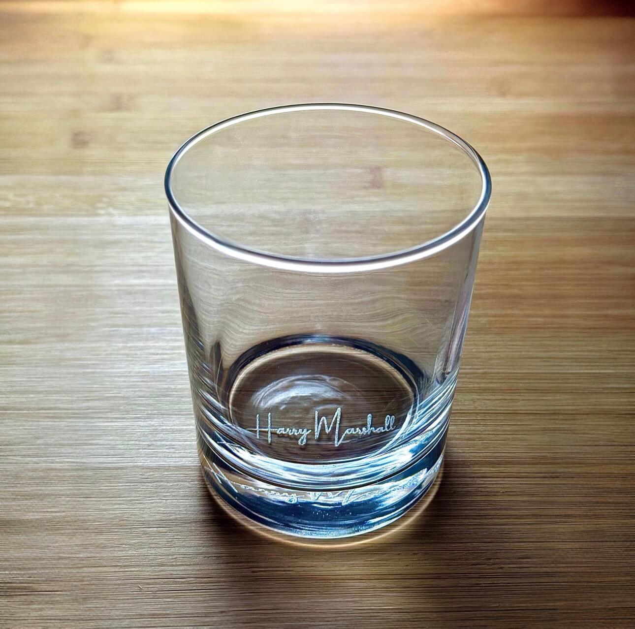Clear side view of engraved whiskey glass showing "Harry Marshall" etched near the base