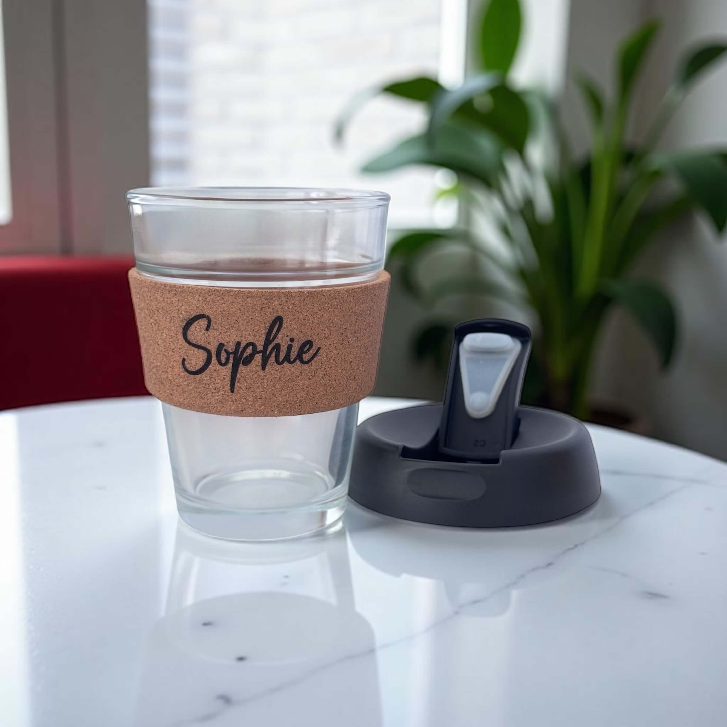 Eco glass coffee cup with cork band engraved Sophie and lid placed next to it