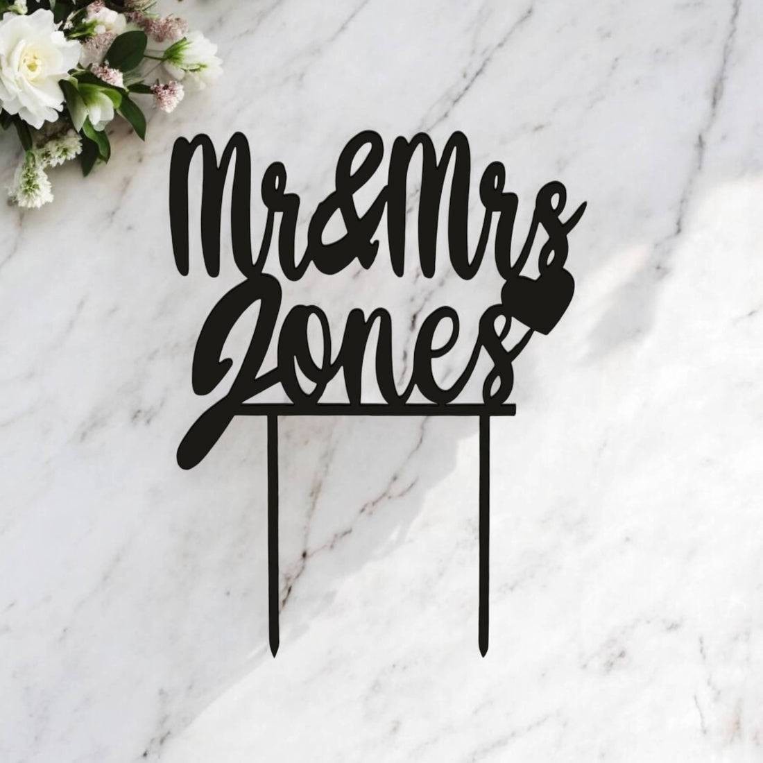 Personalised laser-cut wedding cake topper with custom surname, heart detail and black acrylic finish.