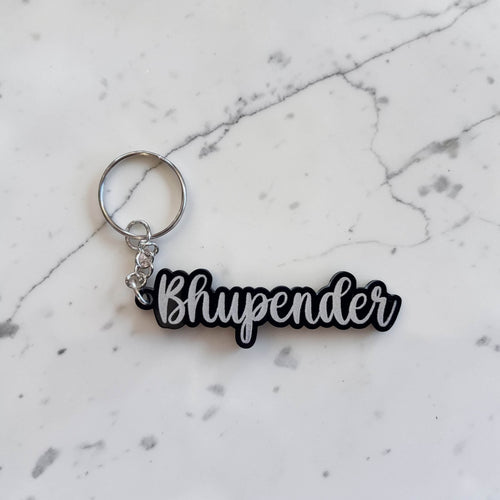 Acrylic keychain with 'Bhupender' text cut-out on a marble surface