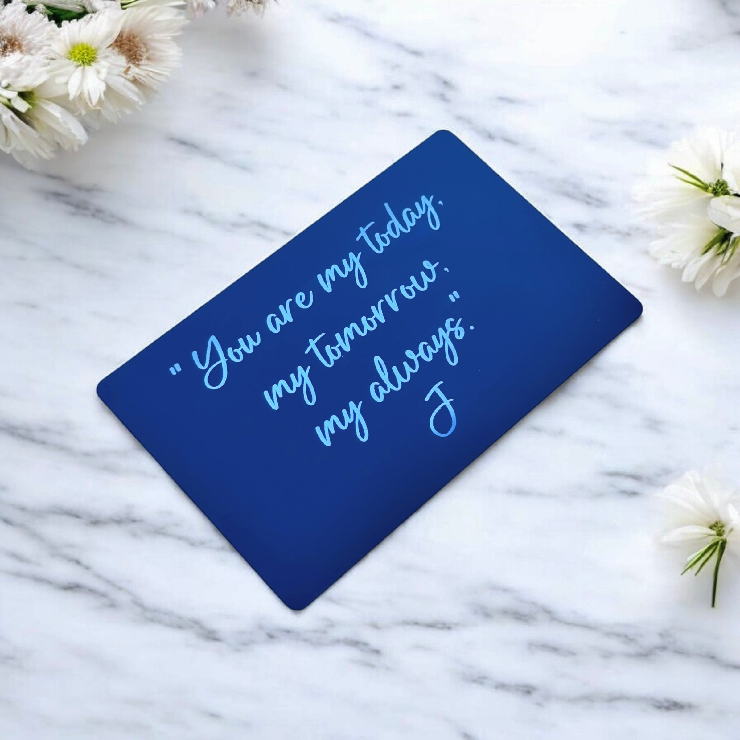 Angled black wallet insert card showing engraved message on white marble surface