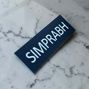 Angled personalised name badge showing white engraved text on a black acrylic front