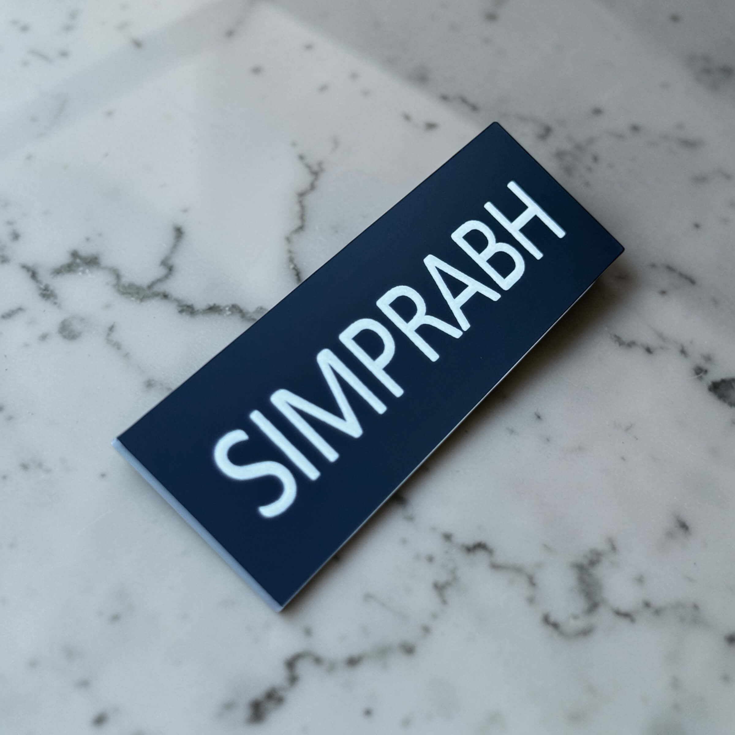 Angled personalised name badge showing white engraved text on a black acrylic front