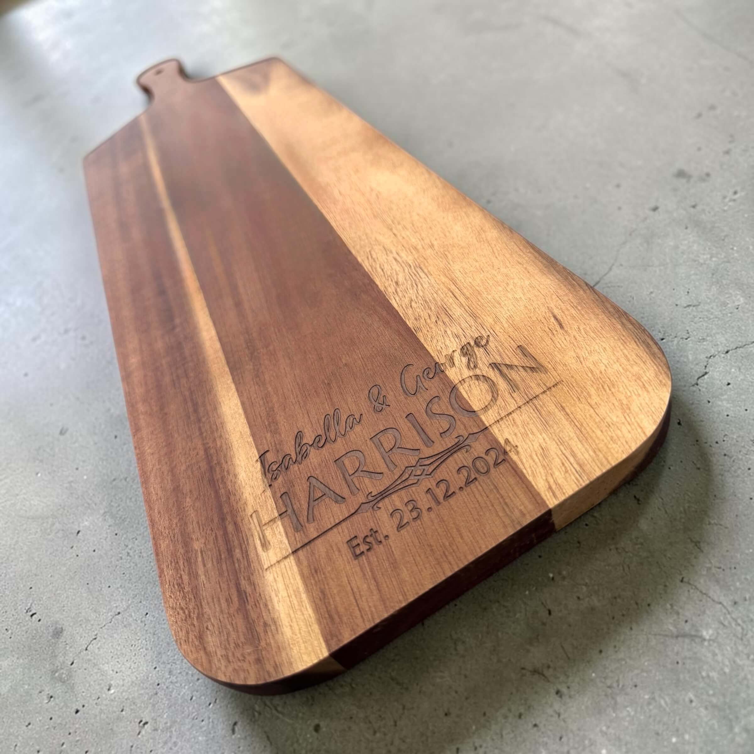 Angled view of a personalised long acacia serve board with two-tone wood grain and engraved couples names and anniversary date