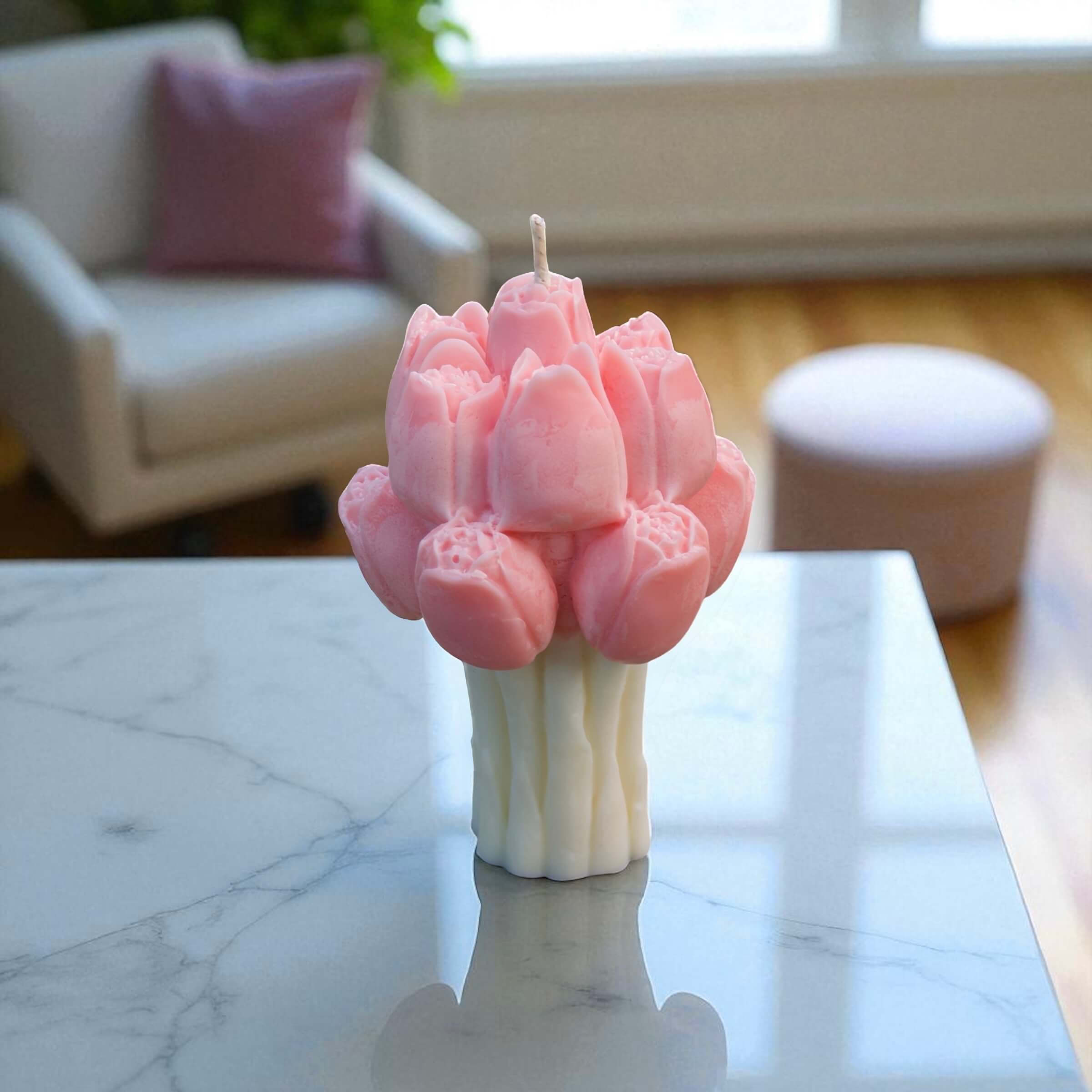Artisan floral candle resembling a bouquet of pink tulips, standing on a glossy marble surface in natural daylight.