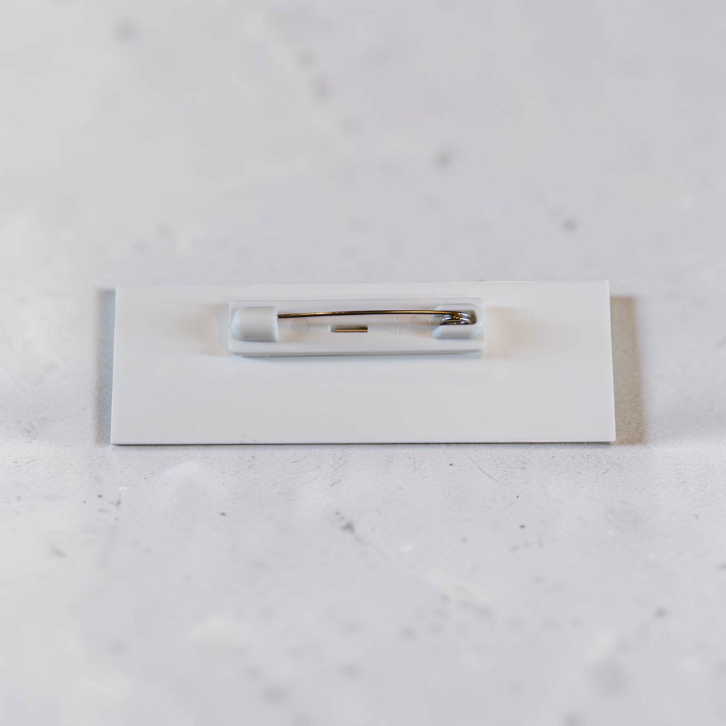 Back of acrylic badge showing white backing and metal pin attachment