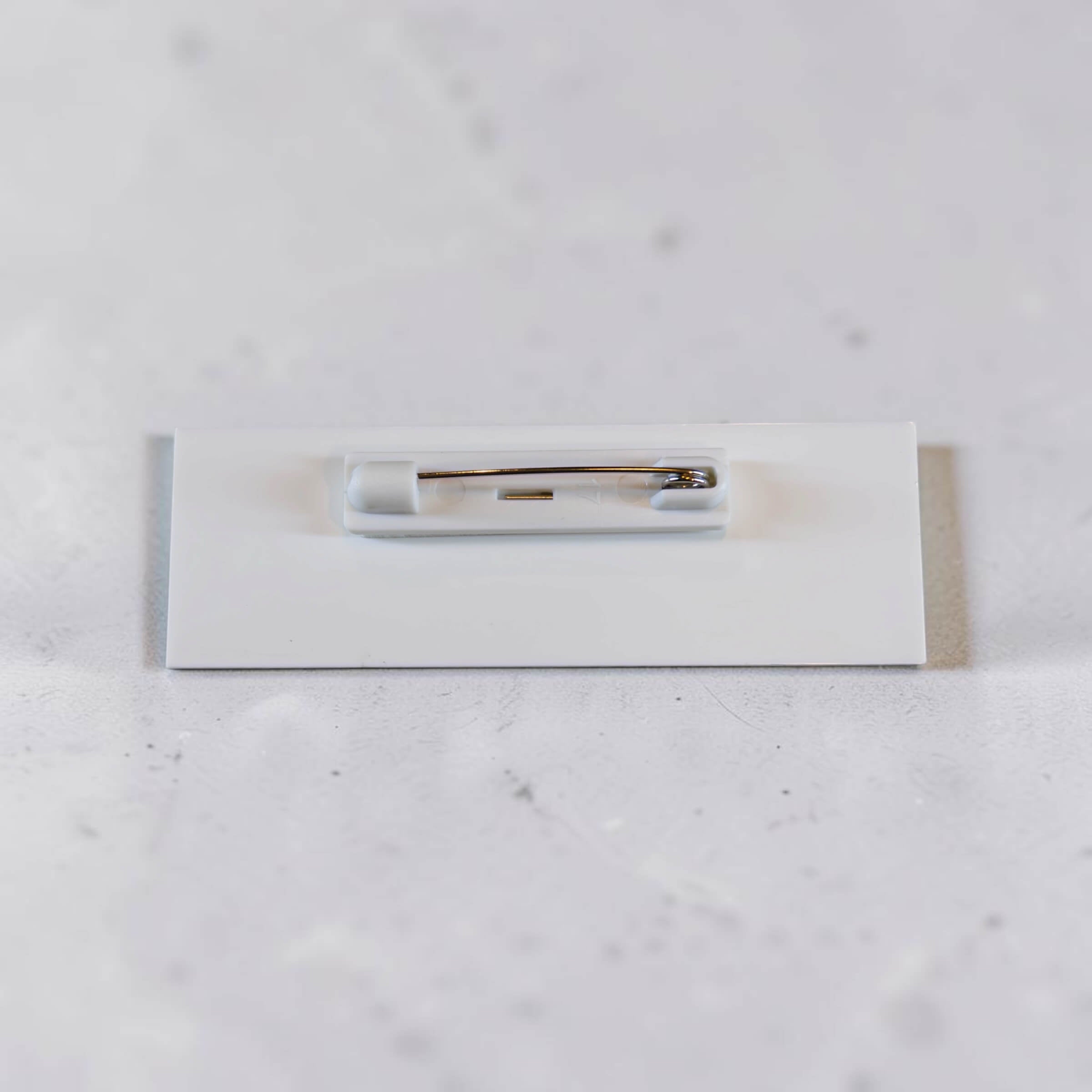 Back of acrylic badge showing white backing and metal pin attachment