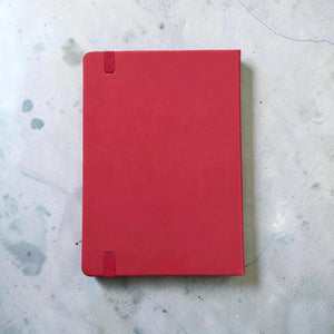Back view of a maroon PU leather A5 notebook with a matching Maroon elastic closure tab, placed on a light gray concrete surface.