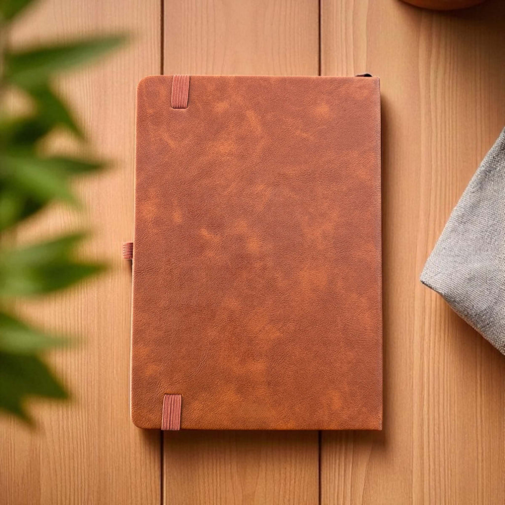 Back view of tan leather planner with elastic band on wooden table