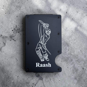 Black custom engraved metal card holder with personalised design and 'Raash' text on a gray concrete surface