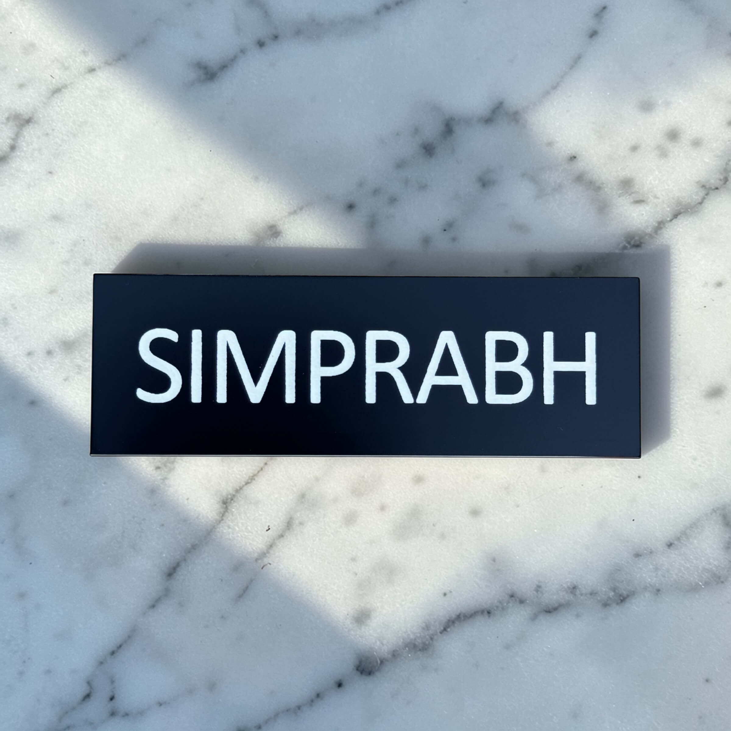 Black custom name badge with pin, engraved with SIMPRABH on a marble surface