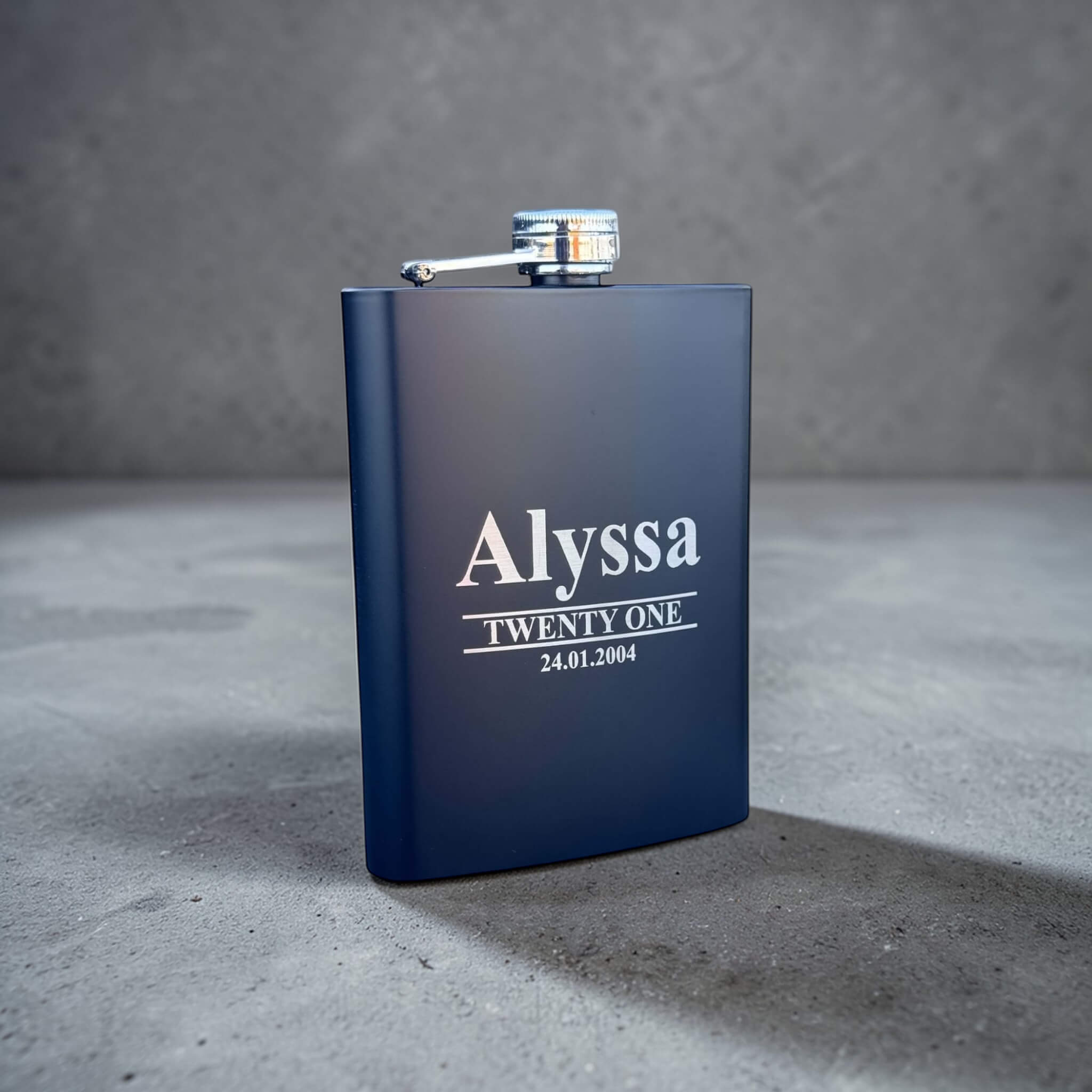 Black engraved 21st birthday hip flask with 'Alyssa Twenty One' text on a gray surface