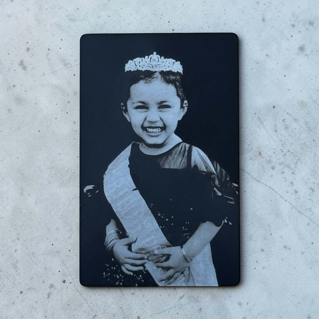 Black engraved photo metal wallet card with child portrait on concrete surface