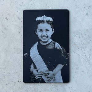 Black engraved photo metal wallet card with child portrait on concrete surface