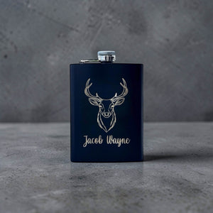 Black flask with deer head design and 'Jacob Wayne' text engraved on a gray surface.
