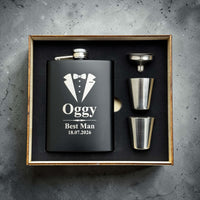 Black hip flask with tuxedo design and personalised text in a wooden box on a gray concrete background