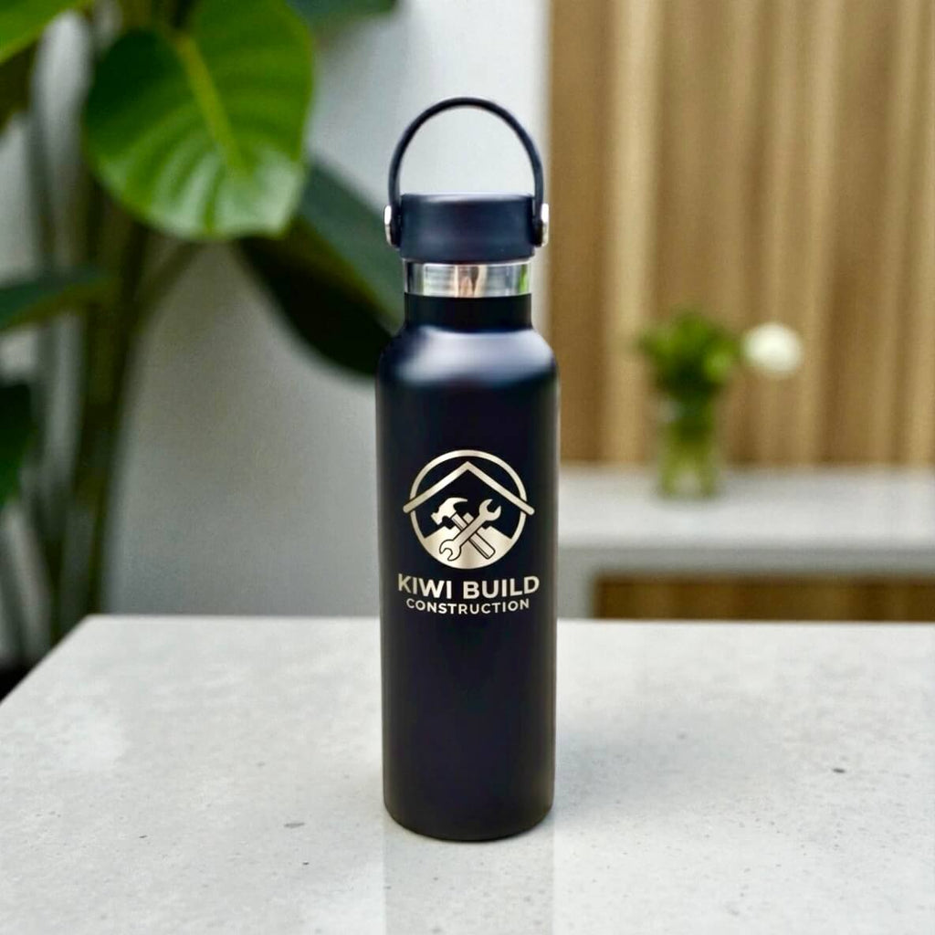 Black water bottle with 'Kiwi Build Construction' logo on a table with a blurred background