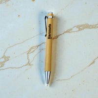 Branded bamboo ballpoint pen with laser engraved Harcourts logo, silver chrome tip and clip, on marble surface