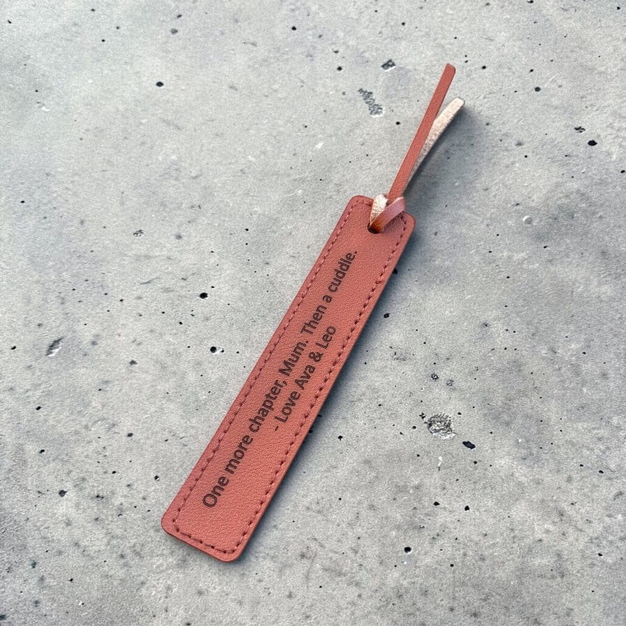 Brown leather bookmark with tassel and engraved text on a concrete surface