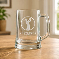 Clear beer mug with engraved Greystone Course golf logo on wooden table