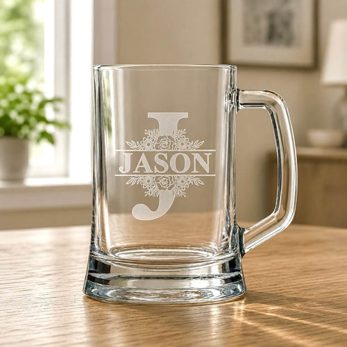Clear glass beer mug with engraved Jason split monogram and floral detail on wooden table