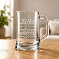 Clear glass beer mug with engraved Ryan 21st birthday design and Brewing Since 2004 on wooden table