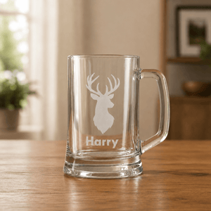 Clear glass beer mug with white stag engraving and the name Harry on a wooden table