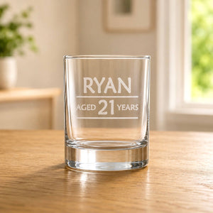 Clear glass shot glass with etched name and age design, shown in warm window light