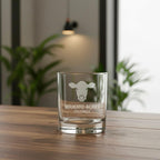 Clear glass with engraved cow logo and text on a wooden surface with a blurred indoor background