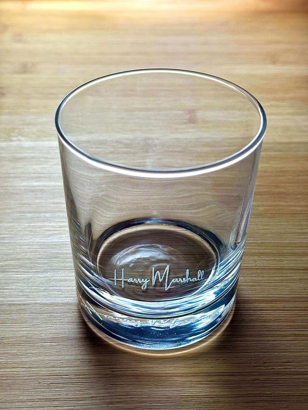 Clear side view of engraved whiskey glass showing "Harry Marshall" etched near the base