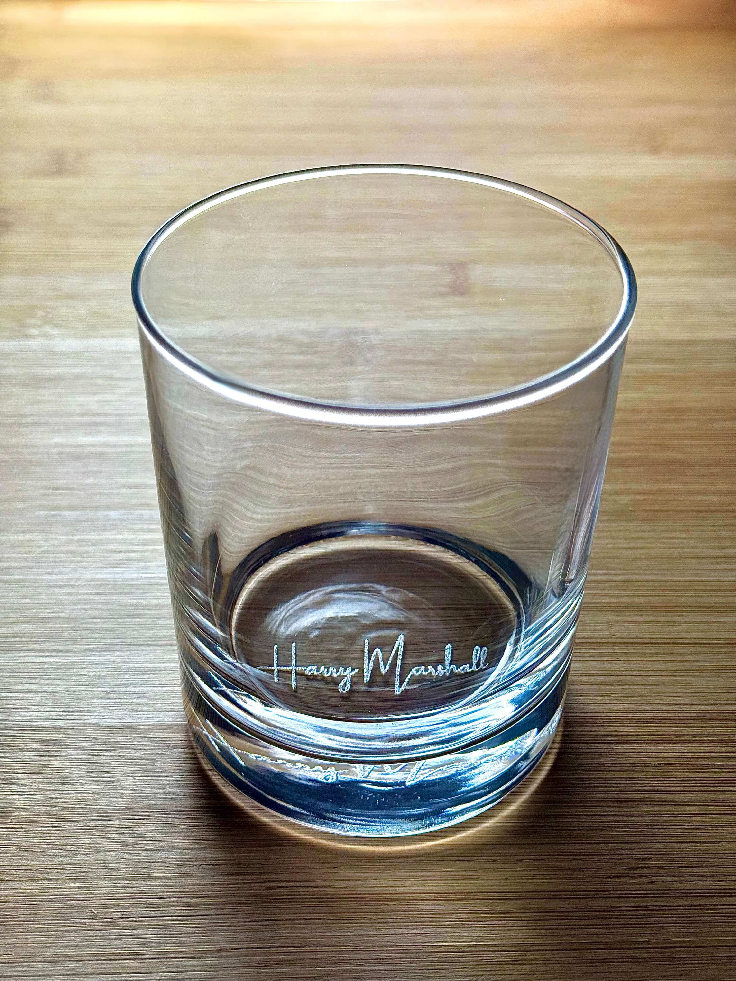 Clear side view of engraved whiskey glass showing "Harry Marshall" etched near the base