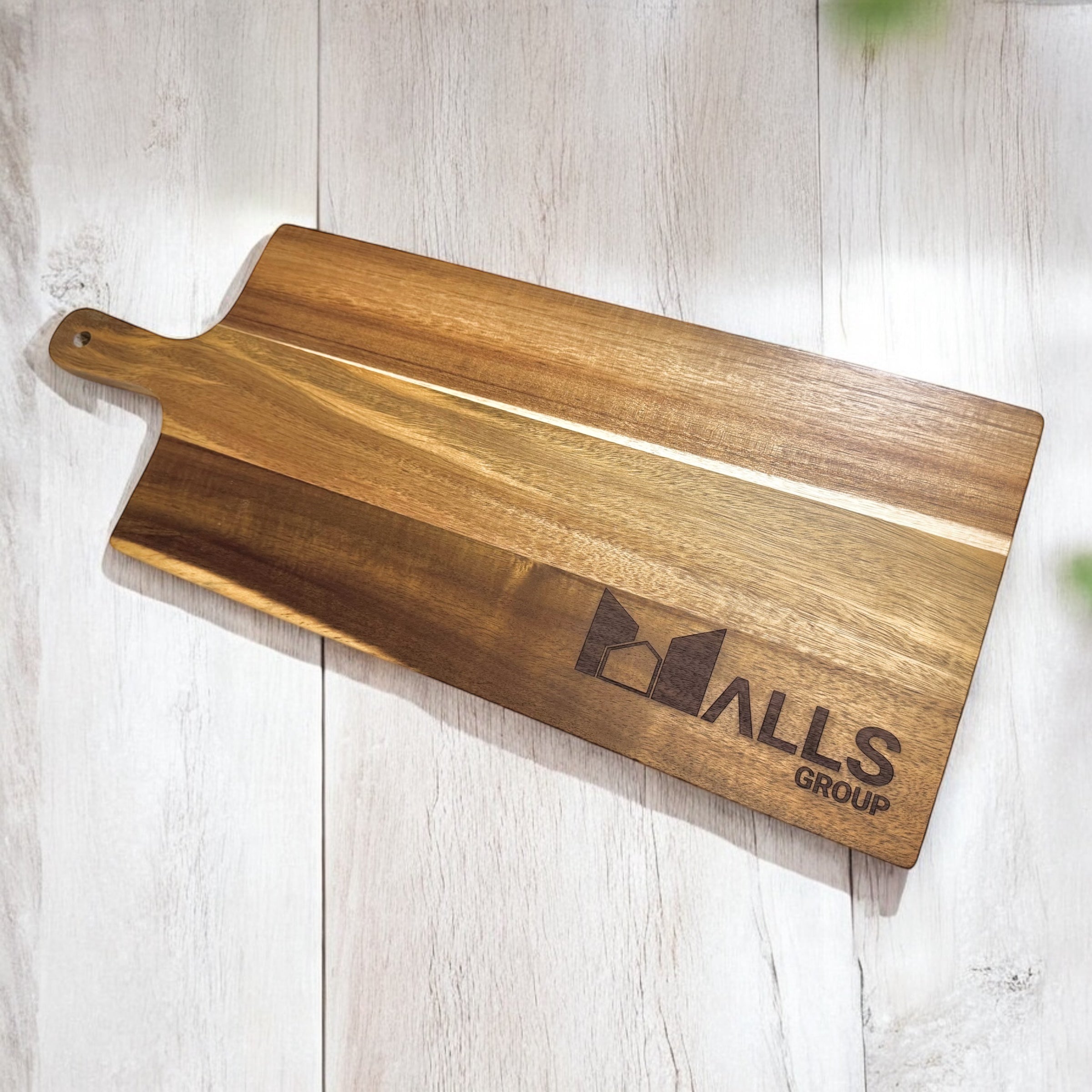 Close-up of acacia serving board engraved with company logo on light wooden surface