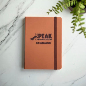 Close-up of custom engraved leather notebook with logo and name showing engraved text detail.