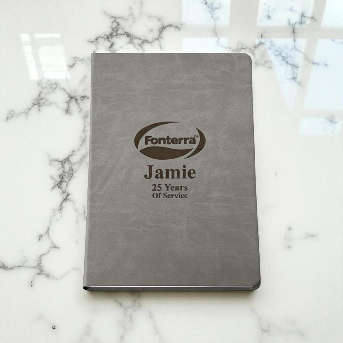 Close-up of custom laser-engraved hardcover notebook showing logo, name, and milestone years of service, perfect for staff recognition gifts.