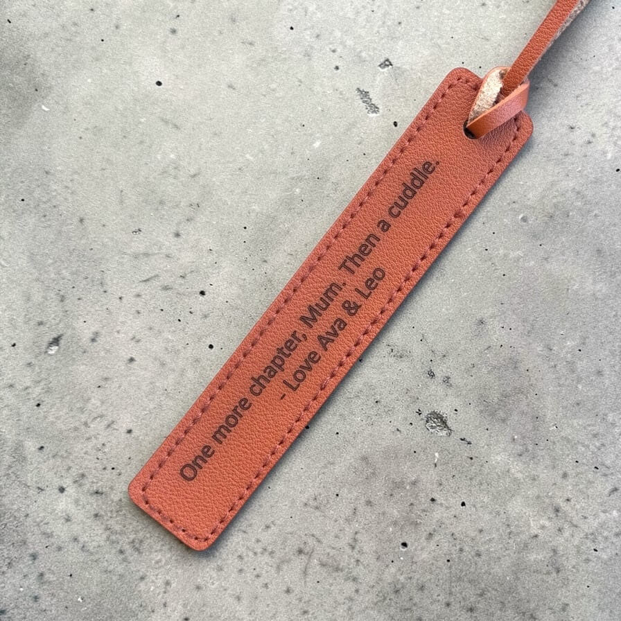 Close-up of engraved message on brown PU leather bookmark with stitched edges on a concrete surface