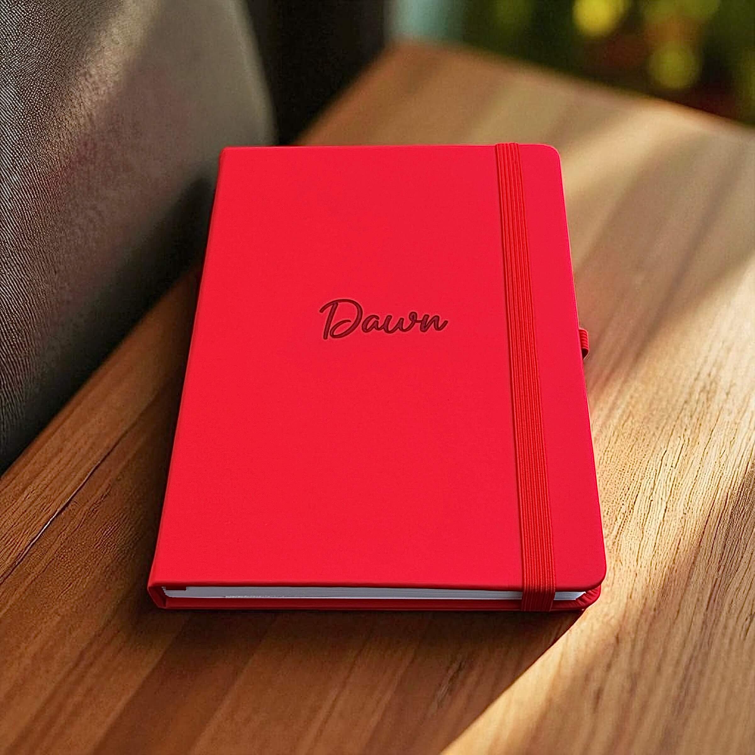 Close-up of red leather notebook with engraved name, elastic closure wrapped neatly around the cover
