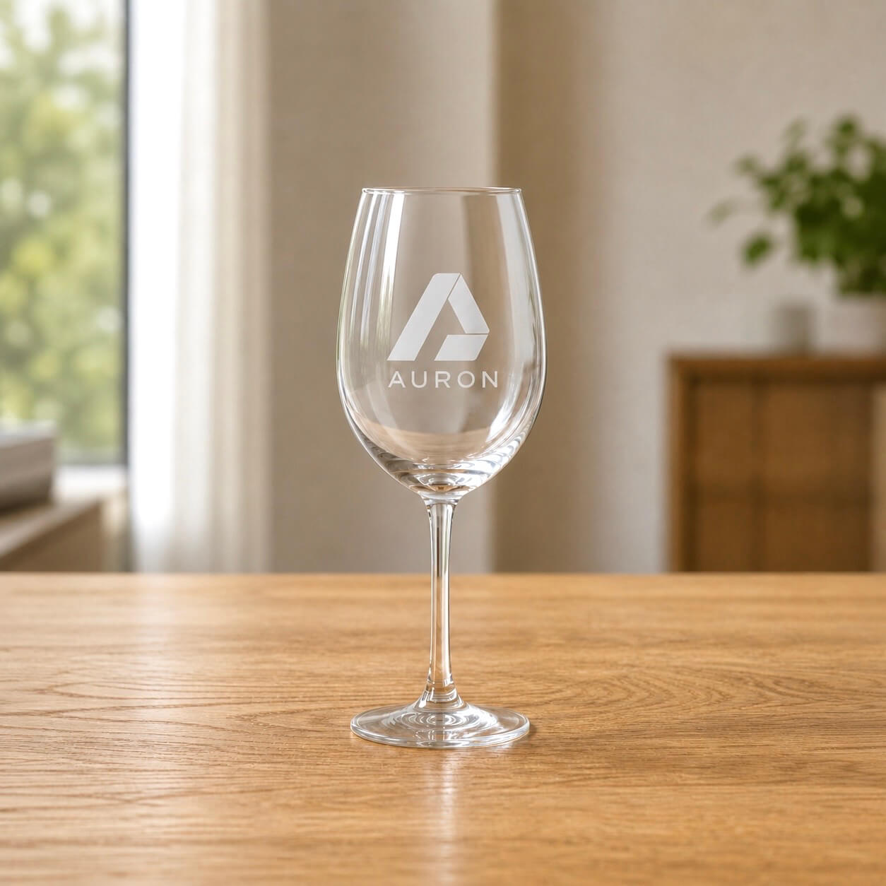 Corporate engraved wine glass featuring the Auron brand logo, photographed on a timber table with natural light