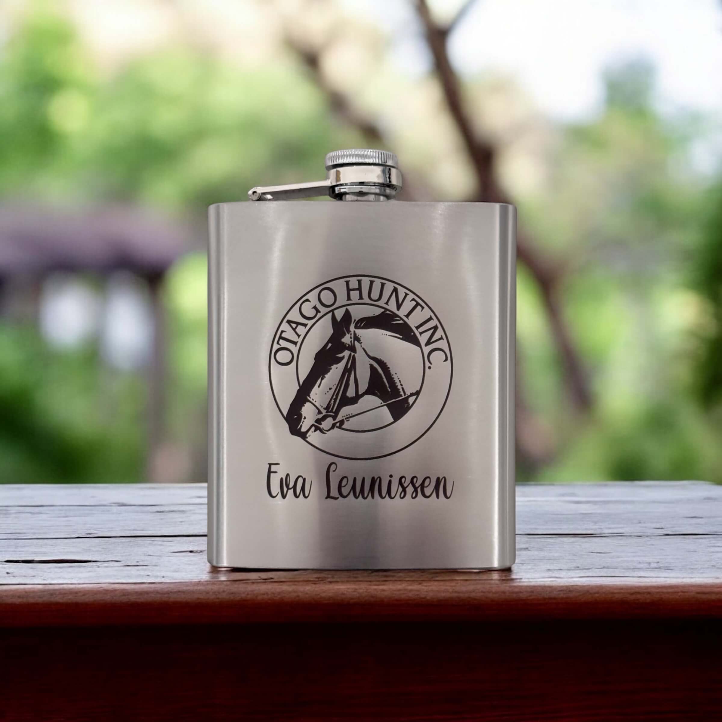 Custom engraved stainless steel flask featuring corporate branding, displayed in natural light.
