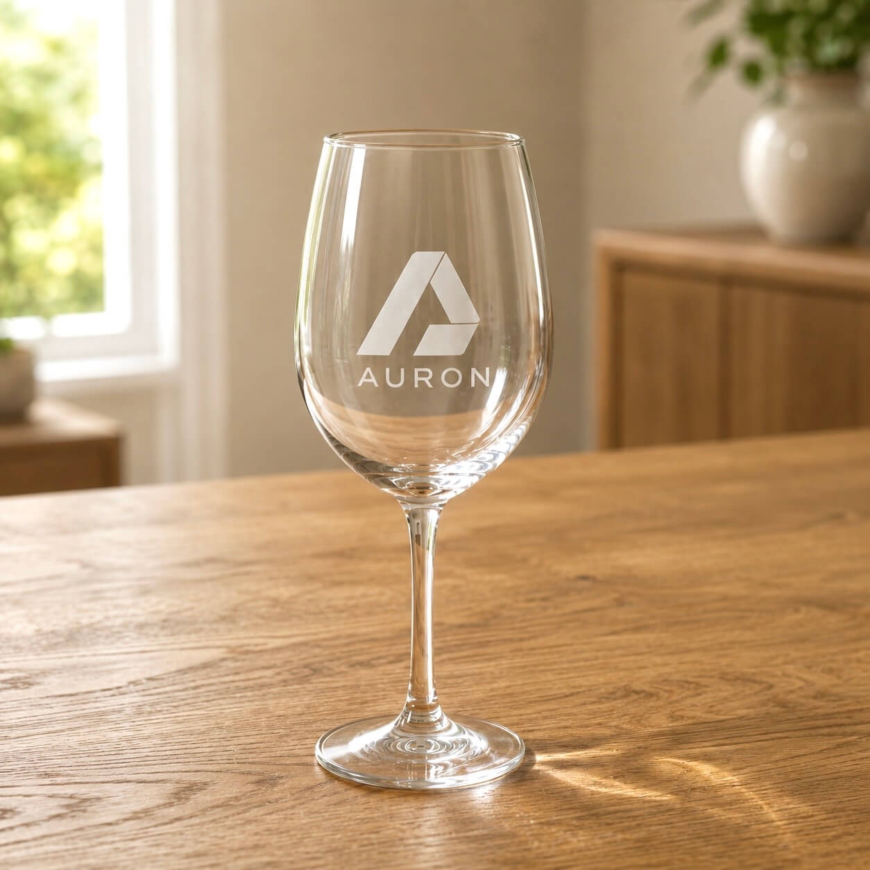 Custom engraved wine glass personalised with a corporate logo for business events, displayed on a wooden table in a warm interior