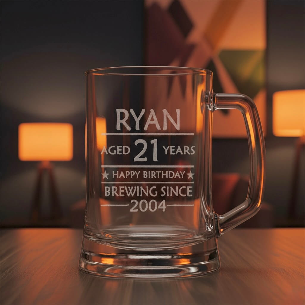 Custom glass beer stein engraved “Ryan 21st Birthday Brewing Since 2004” on dark wooden table in cosy room