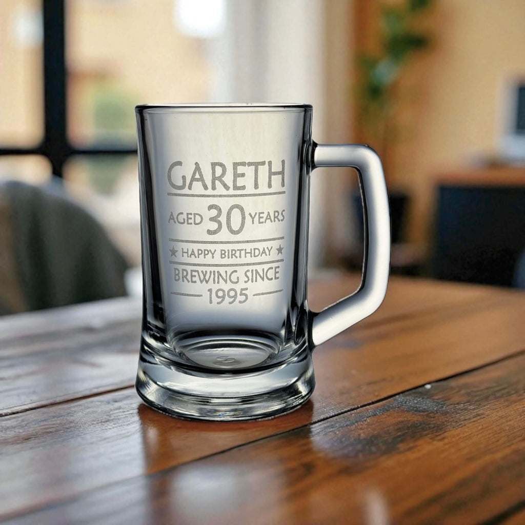 Custom glass beer tankard engraved with birthday message for Gareth, aged 30, on a polished timber surface with a cosy indoor backdrop and soft lighting