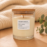 Custom scented soy candle in clear glass jar with Creamy Vanilla label and wooden lid