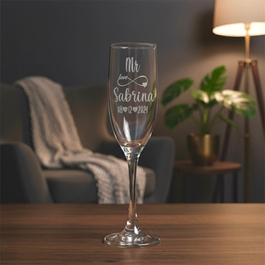 Elegant engraved wedding champagne glass with name and date, displayed on wooden table in cosy home setting.