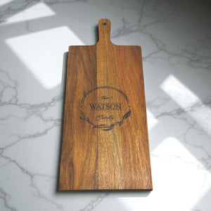 Engraved family serving board with handle, warm wood grain and natural sunlight