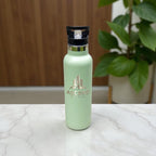 Engraved sage green corporate drink bottle shown on marble surface with indoor plant background.