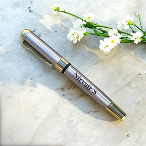 Engraved silver pen with gold accents on a marble surface with white flowers