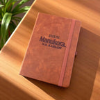 Flat-lay of the engraved leather planner on a sunlit desk, highlighting the bold Manukora branding and professional design