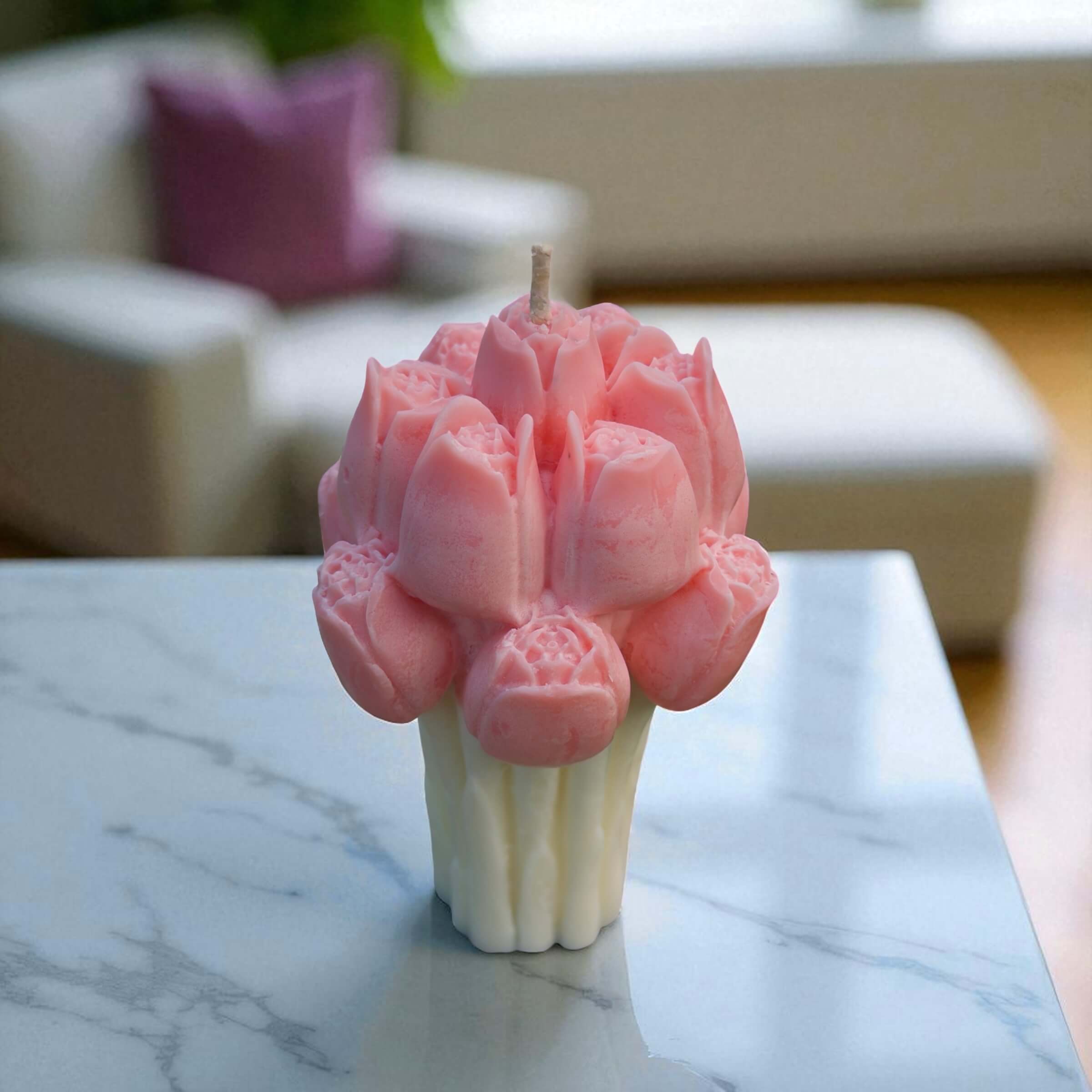 Handcrafted pink tulip bouquet-shaped candle with white stem base, displayed on a marble tabletop in a modern living room.