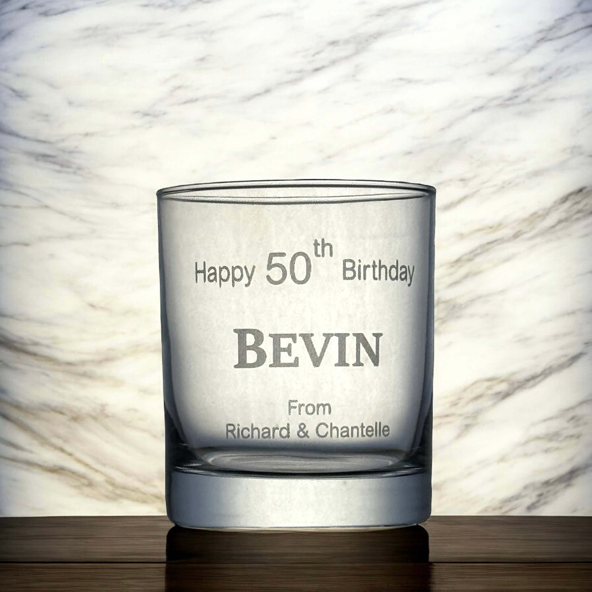 Laser-etched birthday whiskey glass on a wooden surface, featuring a custom name and message.