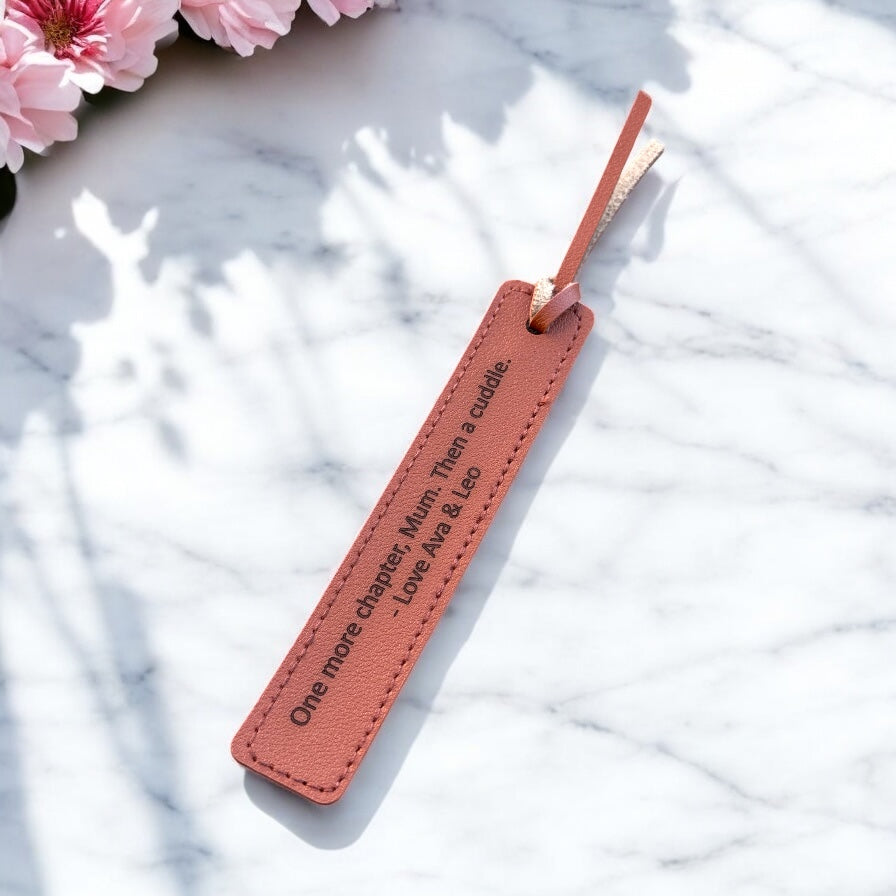 Leather bookmark with engraved quote and tassel beside pink flowers.